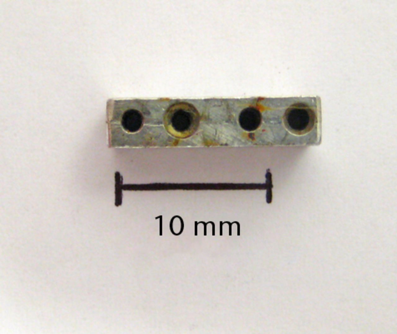 Figs. 1a - 1b 
              Photographs showing the custom-made
four-hole jig, showing a) the superior surface, and b) the lateral
surface, with two holes used for threading of fine wire to help
secure the jig onto bone. There is also a roughened inferior surface
(not seen) to prevent the jig slipping on bone during drilling.
            