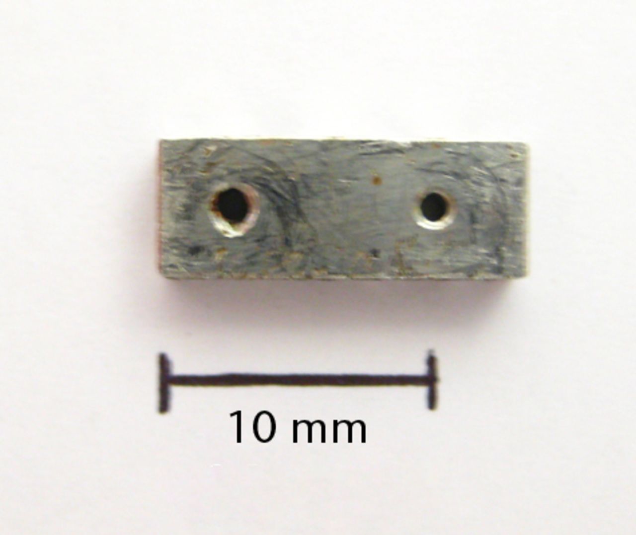 Figs. 1a - 1b 
              Photographs showing the custom-made
four-hole jig, showing a) the superior surface, and b) the lateral
surface, with two holes used for threading of fine wire to help
secure the jig onto bone. There is also a roughened inferior surface
(not seen) to prevent the jig slipping on bone during drilling.
            